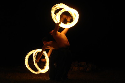 Fire spinners love to see pictures of themselves in action, and it hard to make an exposure the right speed to catch both the spinners and the fire.  Here the pair of them held their position for the 3/4 of a second at F6.3 I used to make the picture.   As you can see, though, the details of the bodies and faces are nearly impossible to make out.

Plus, more often than not, the autofocus will not work under conditions like these, and using the manual focus, either through the viewfinder or peering at the LCD is only marginally better since the dancers are not usually standing in one place long enough to work the manual focus.  So I generally use the only approximately accurate distance indicated on my screen and turn the manual focus dial until the distance indicated is about what I estimate it to be.