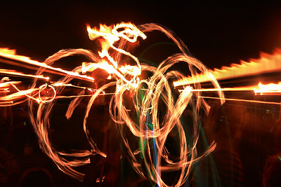 While the blur introduced by zooming can make for a very interesting image, and fire is fascinating, there are essentially only two colors: yellow and black.  Fire dancers usually learn their moves by practicing with color lights and in this picture we get a hint of color from a neophyte spinning lights while behind him someone else is spinning fire.  

Working with colored lights leads to another set of exposure problems, and sometimes much more interesting images.